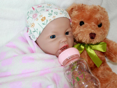 A baby doll lying on a bed next to a plush stuffed animal, evoking a sense of comfort and childhood innocence.